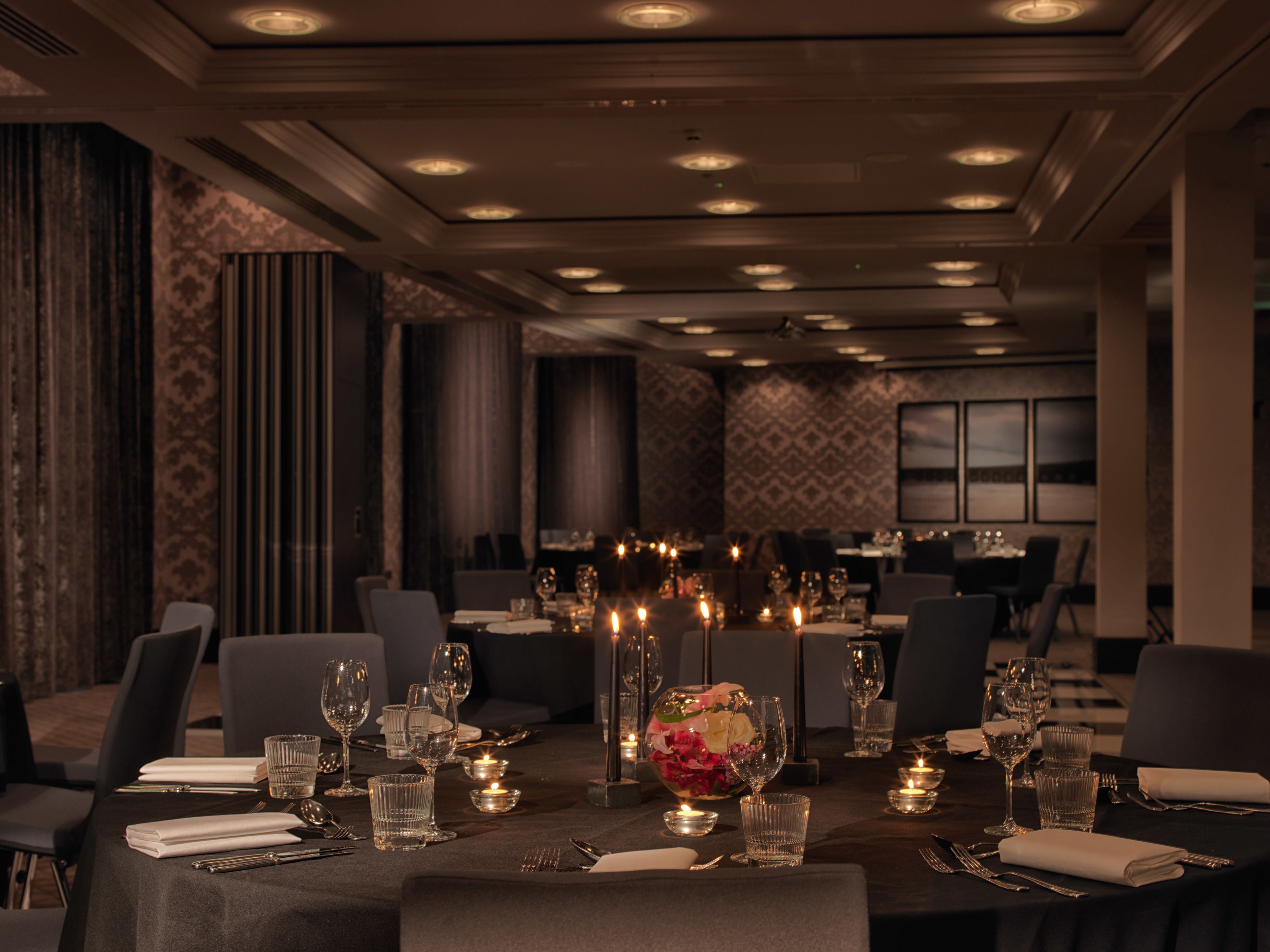 Un restaurante tenuemente iluminado con mesas dispuestas para comer, velas y un centro de mesa floral.