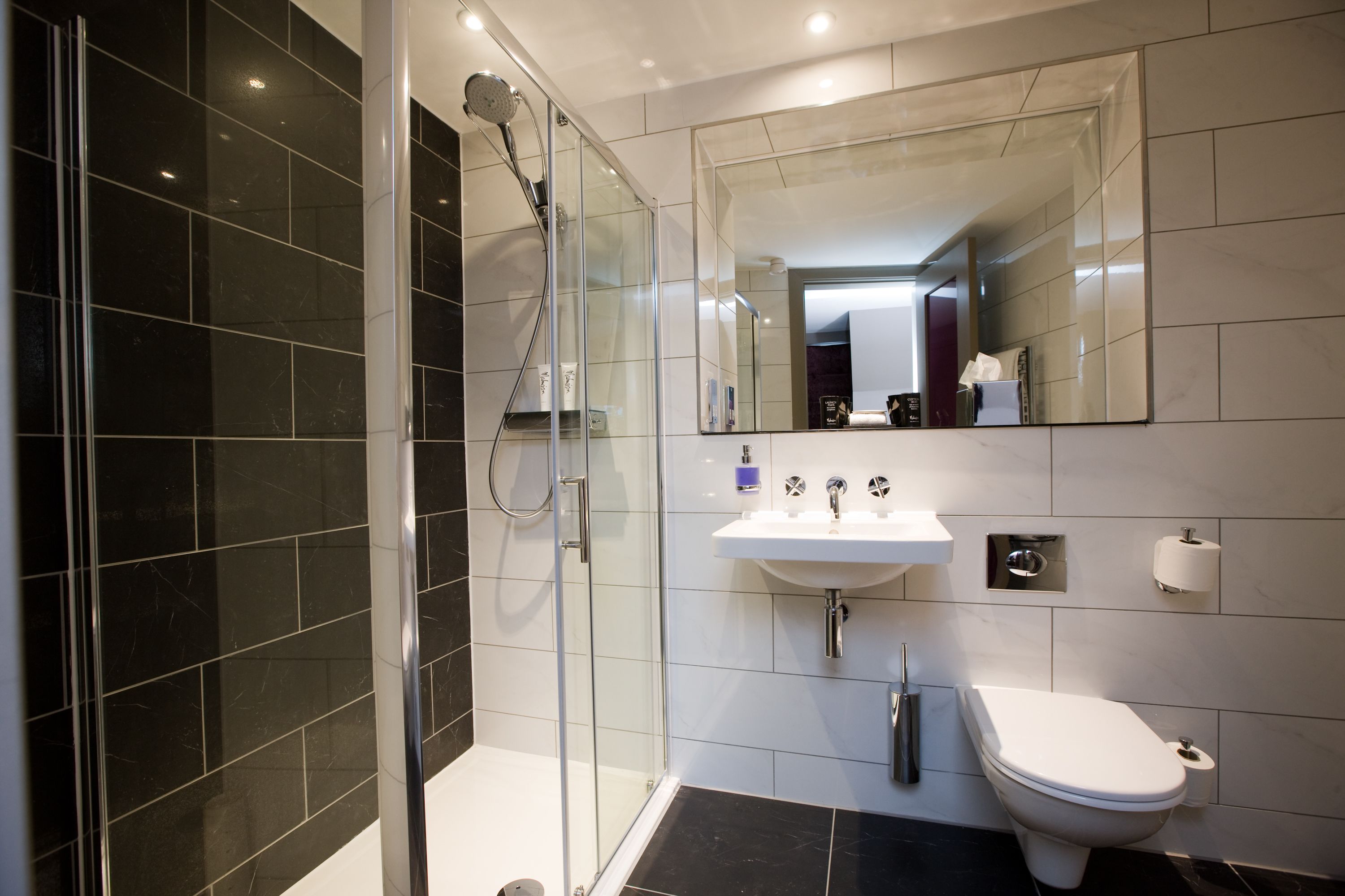 Een moderne badkamer met een glazen douchecabine, een wit wastafelmeubel en een toilet.
