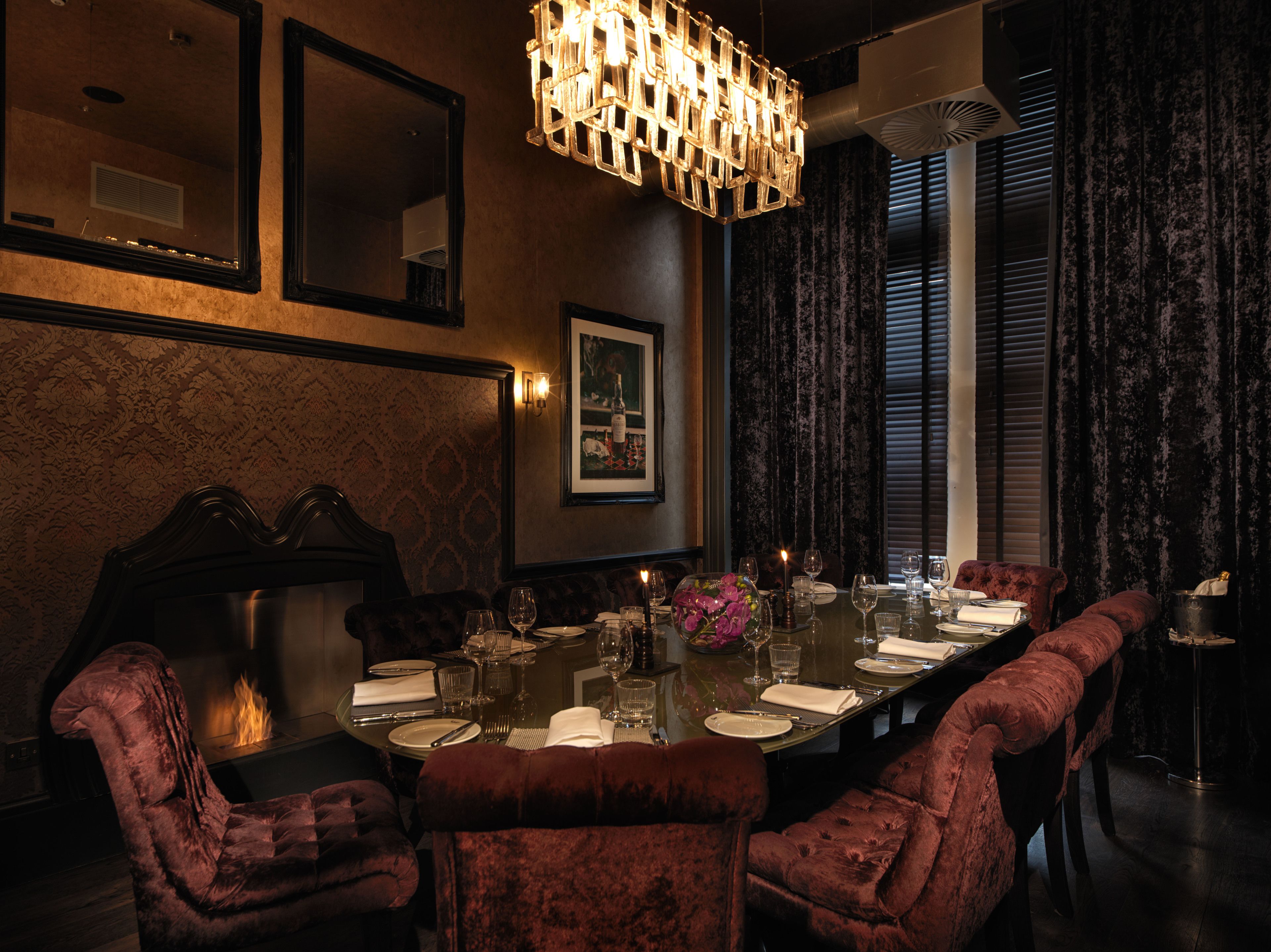 A formal dining room with a long table, plush red upholstered chairs, and a modern chandelier.