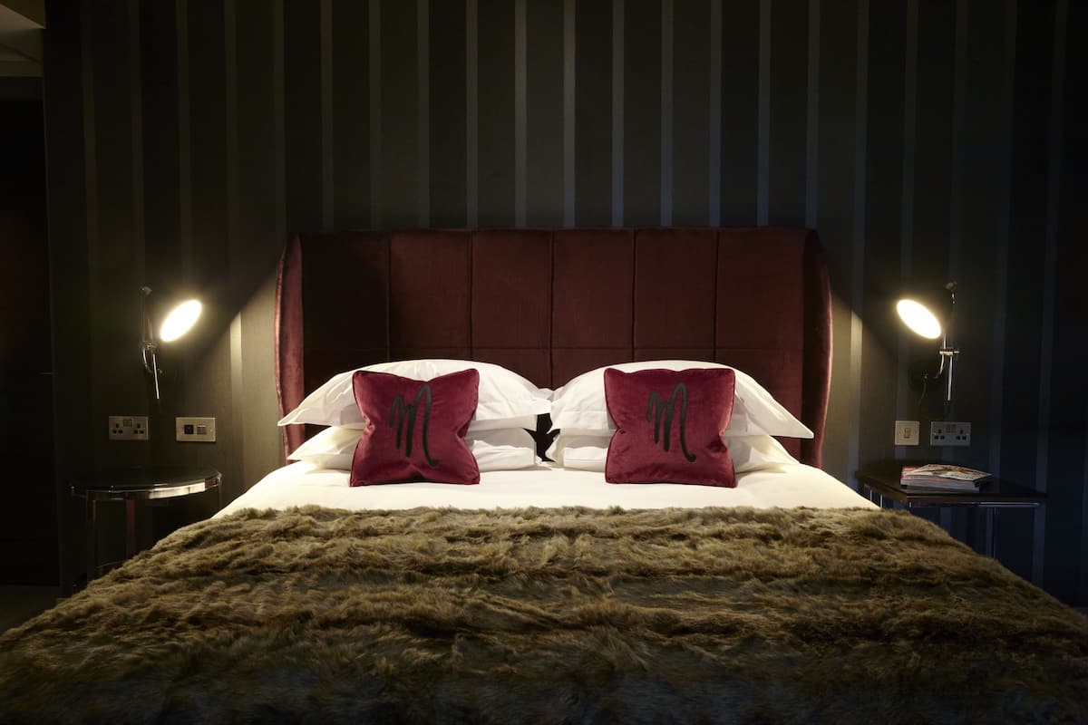 Ein ordentlich bezogenes Bett mit einer flauschigen Decke, zwei Kissen mit einem Logo und zwei Nachttischlampen.
