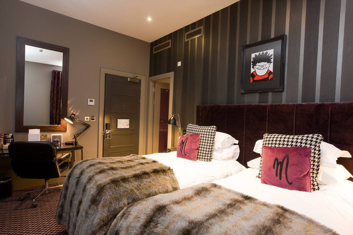 Ein Hotelzimmer mit Bett, Schreibtisch, Stuhl, Spiegel und einem gerahmten Bild an der Wand.