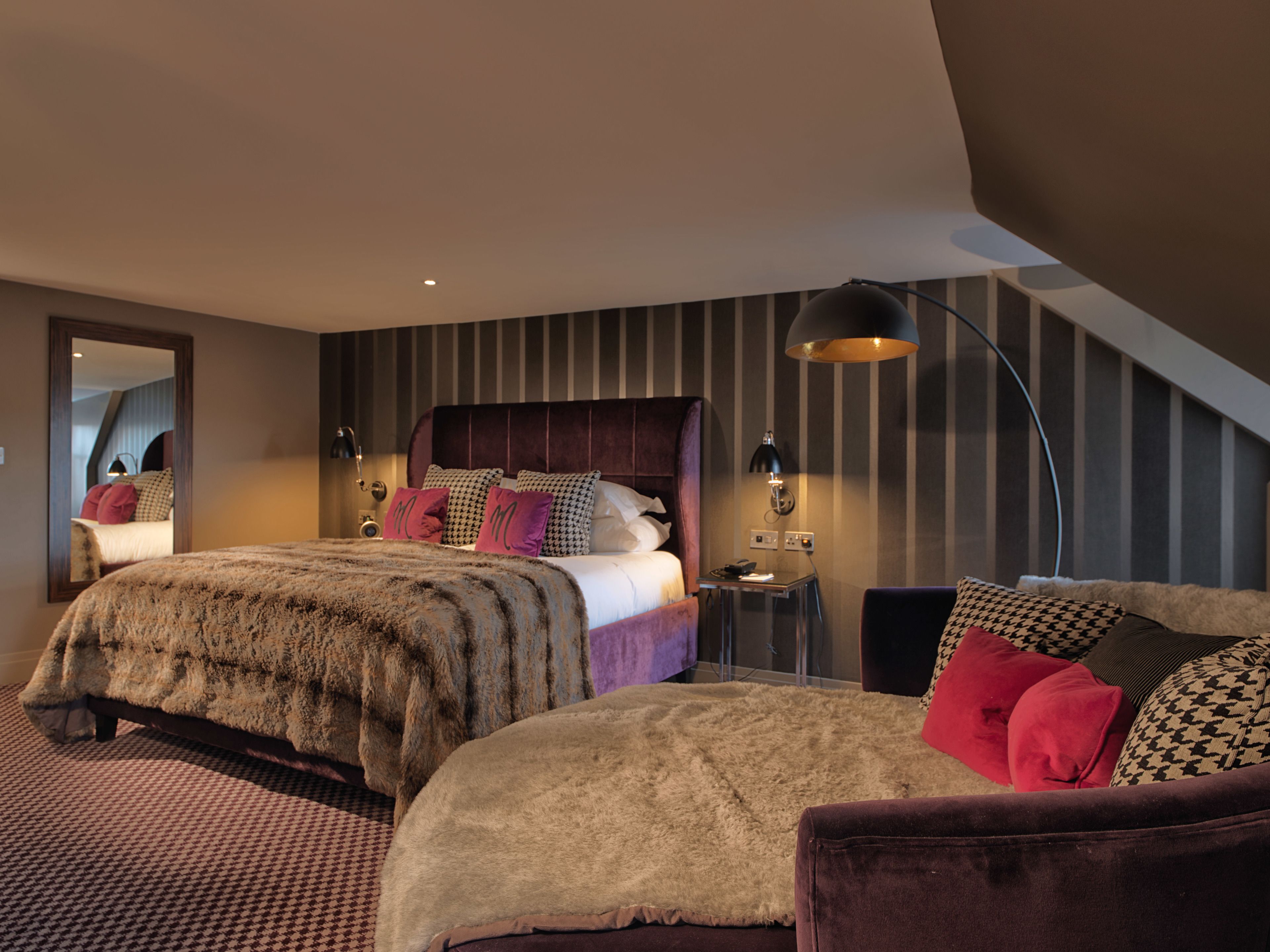 A modern bedroom with a large bed, a smaller bed, a desk, and a chair.