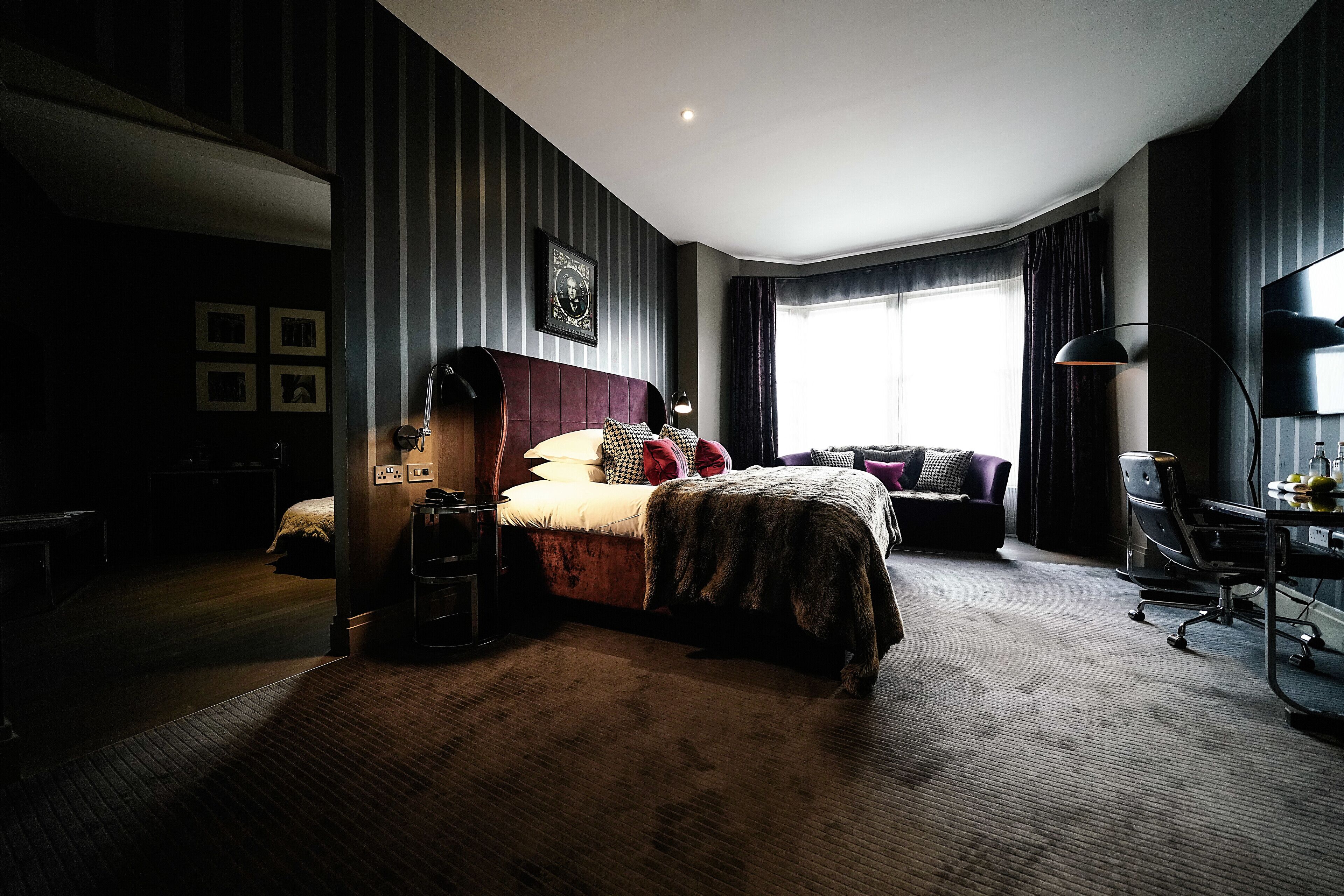A modern hotel room with a large bed, a desk, and a chair. There is a window with curtains and a picture on the wall.