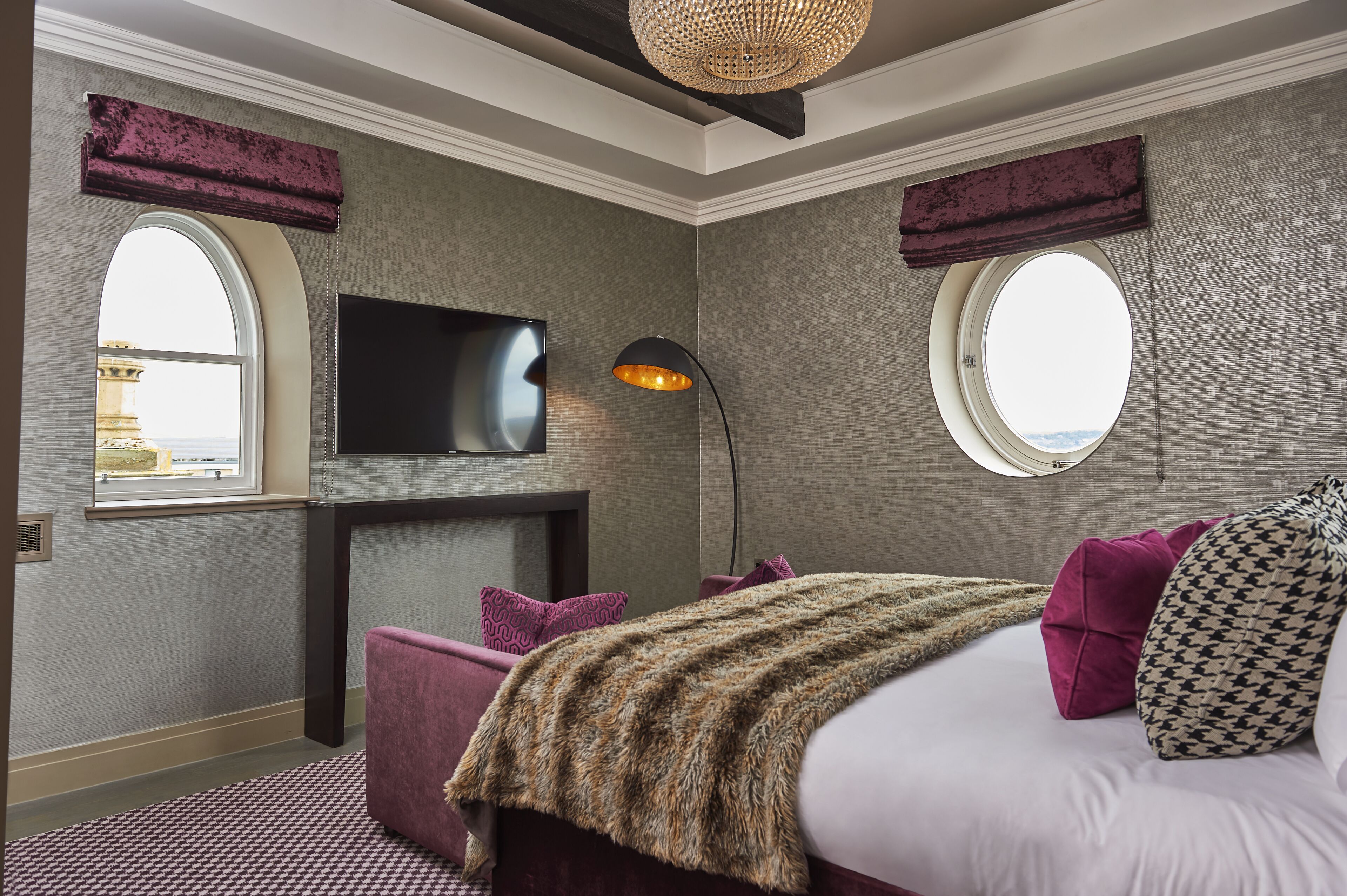 A bedroom with a large bed, two windows, a flat-screen TV, and a fireplace.