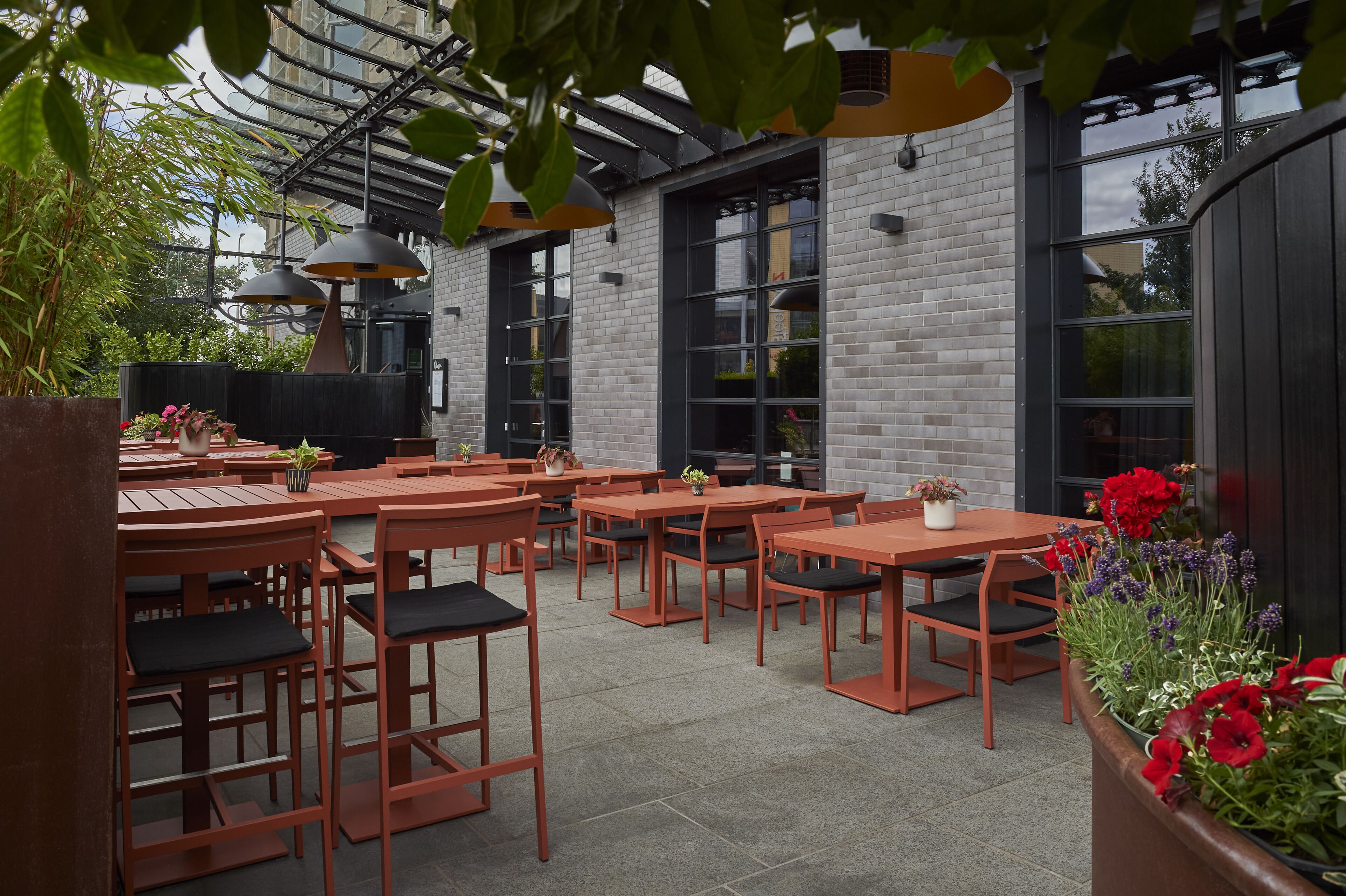 An outdoor seating area with tables and chairs, surrounded by brick walls and large windows.