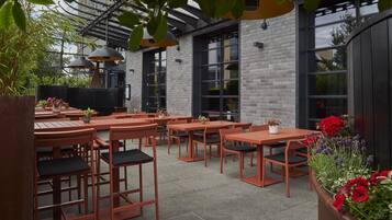 An outdoor seating area with tables and chairs, surrounded by brick walls and large windows.