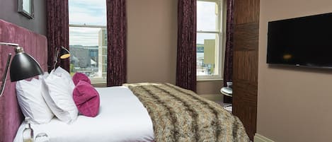 A hotel room with a large bed, a TV, a bedside table with a lamp, and a window with curtains.