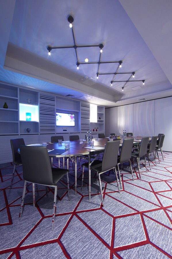 Una sala de conferencias con una mesa larga, sillas, una pantalla de proyector y una alfombra de diseño geométrico.