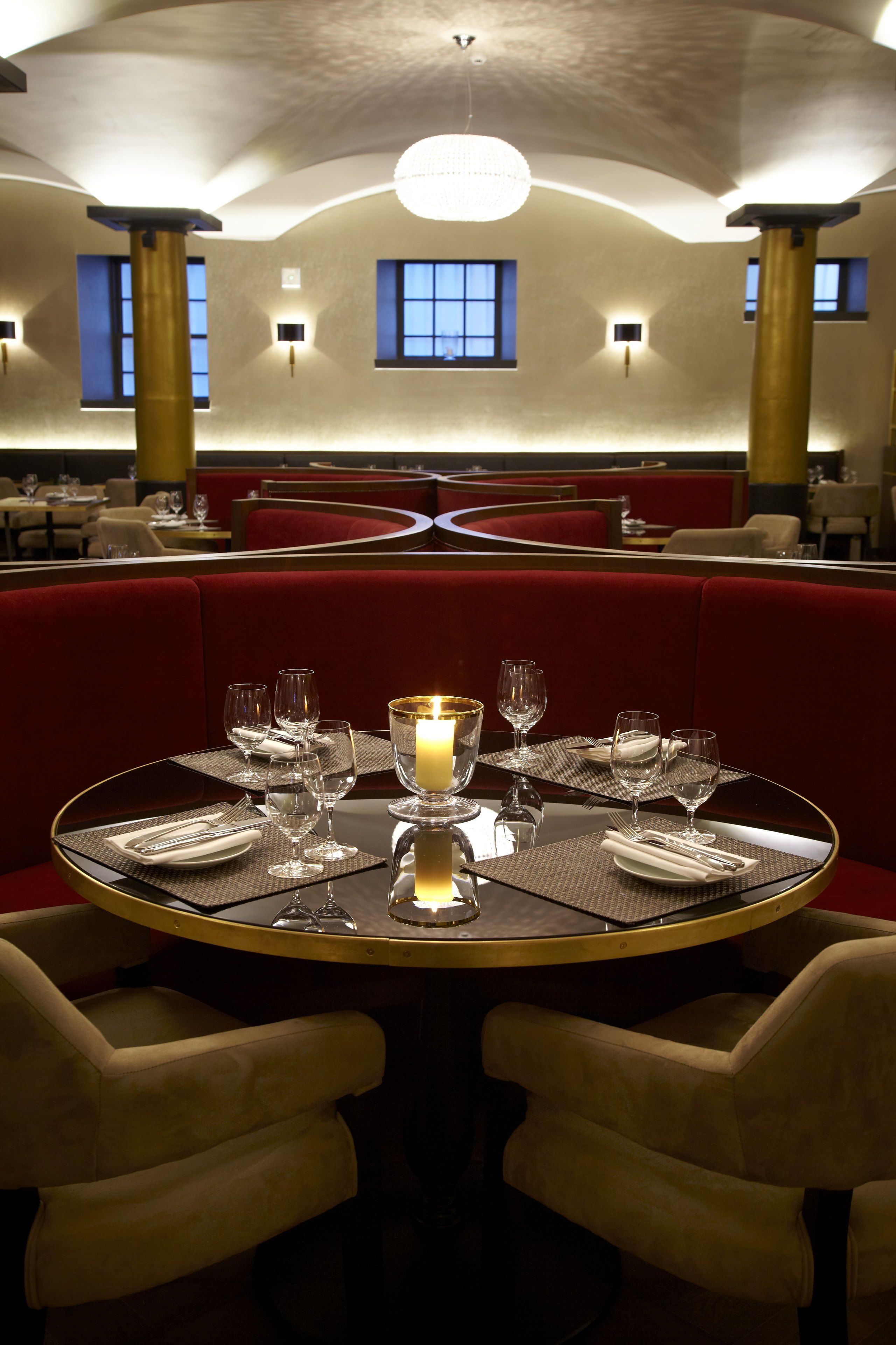 Un restaurante con mesas redondas, asientos tapizados en rojo y un candelabro.