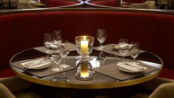 Un restaurante con mesas redondas, asientos tapizados en rojo y un candelabro.