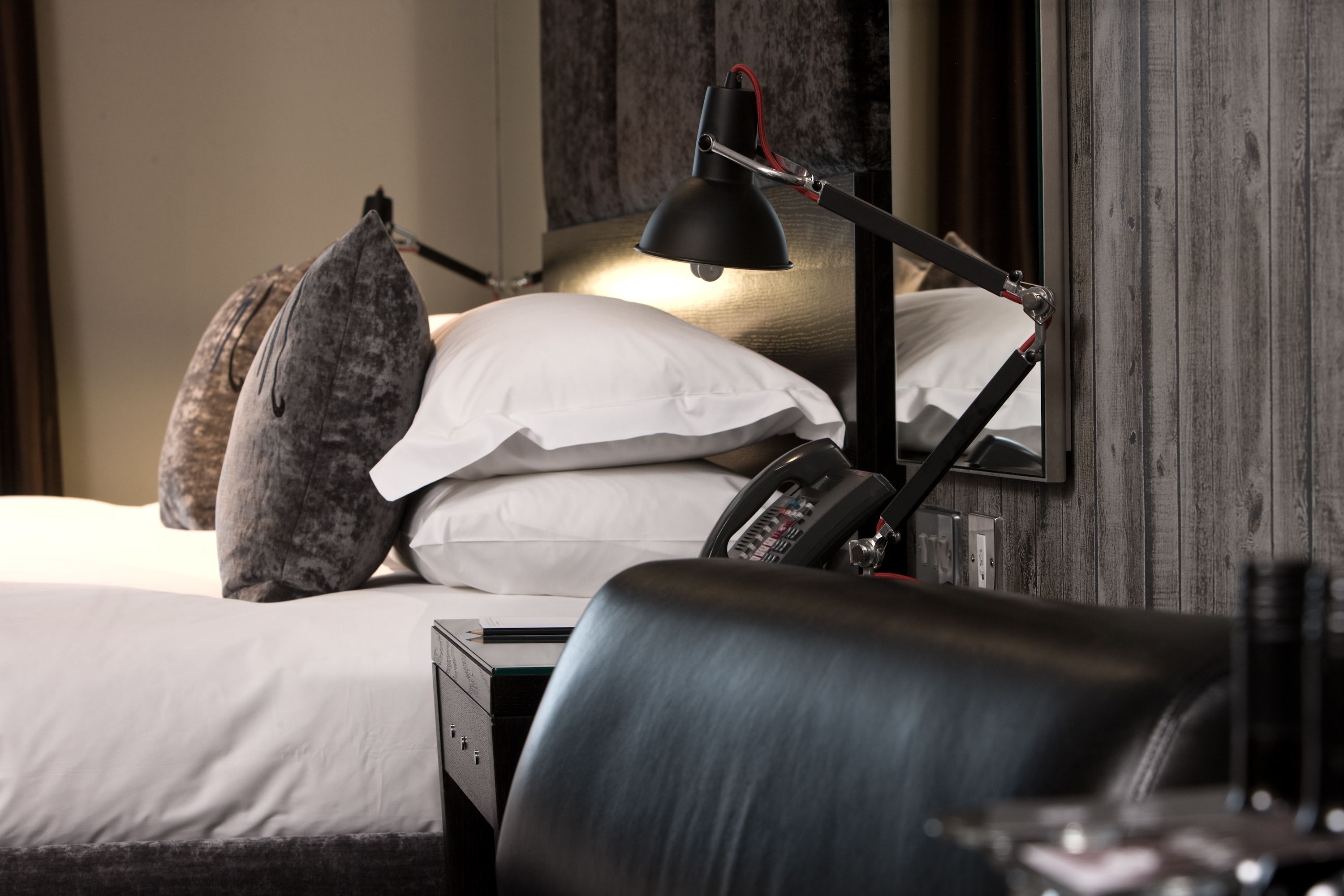 Ein ordentlich bezogenes Bett mit weißen Laken, eine schwarze Schreibtischlampe und ein Telefon auf dem Nachttisch.