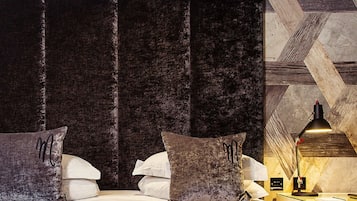 A modern bedroom with a large bed, dark upholstered headboard, and a geometric patterned ceiling.