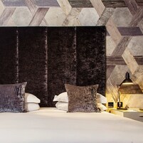 Un dormitorio moderno con una cama grande, cabecera tapizada en tonos oscuros y techo con estampado geométrico.