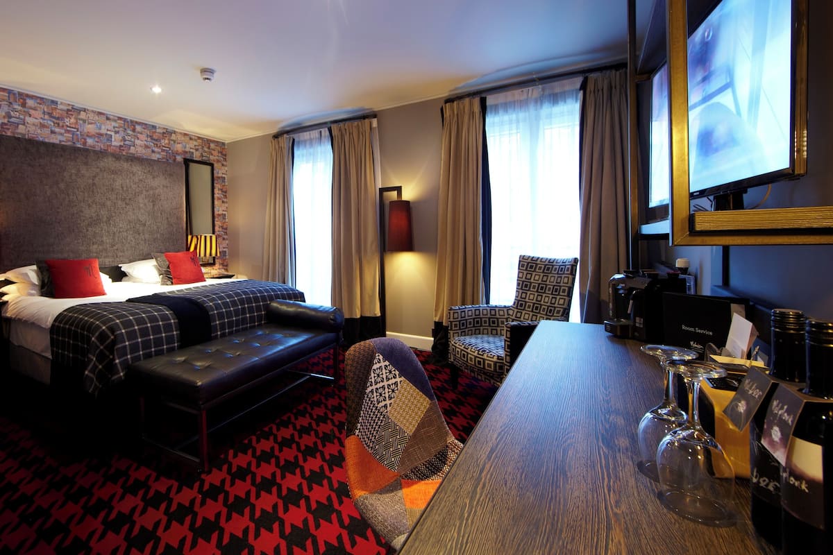 A hotel room with a bed, a sofa, a desk, a chair, a TV, and a coffee machine.