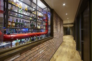 A bar area with shelves of liquor bottles, a red pipe, and a brick wall.