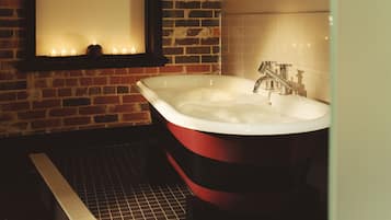 Un baño con una bañera roja y blanca, suelo de baldosas y pared de ladrillo.