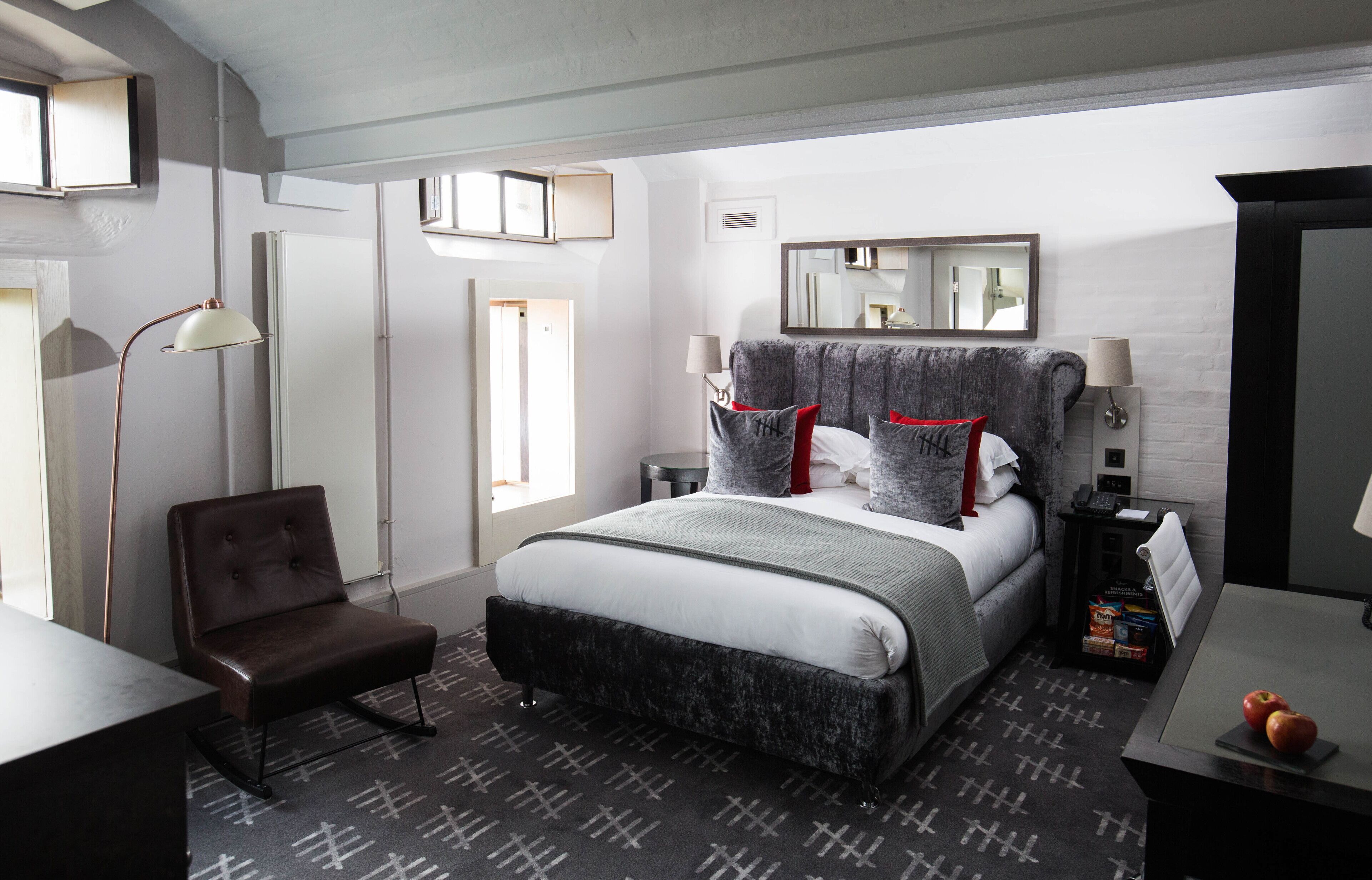 A modern hotel room with a large bed, a desk, a chair, and a small table with apples.