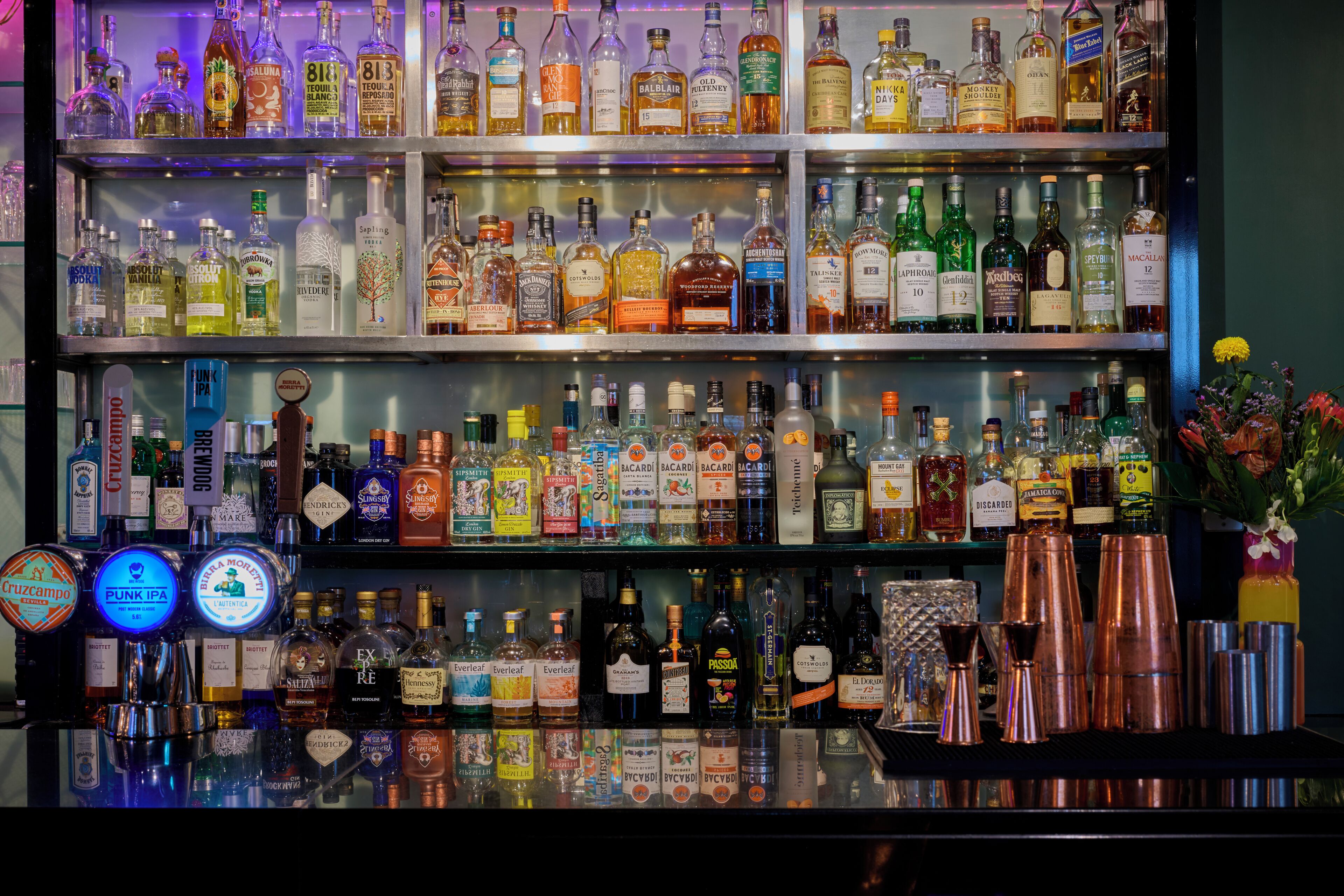 Un bar doté de plusieurs étagères remplies de bouteilles d’alcool et d’une variété d’ustensiles de bar disposés sur le comptoir.