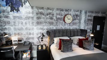 A hotel room with a bed, a desk with a telephone, a chair, a trash bin, and a wall clock.
