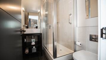Un baño moderno con ducha envuelta en vidrio, inodoro blanco y tocador negro con espejo.