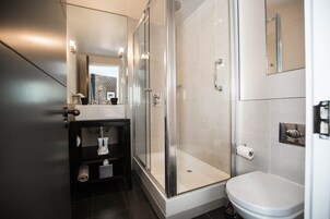 Un baño moderno con ducha envuelta en vidrio, inodoro blanco y tocador negro con espejo.