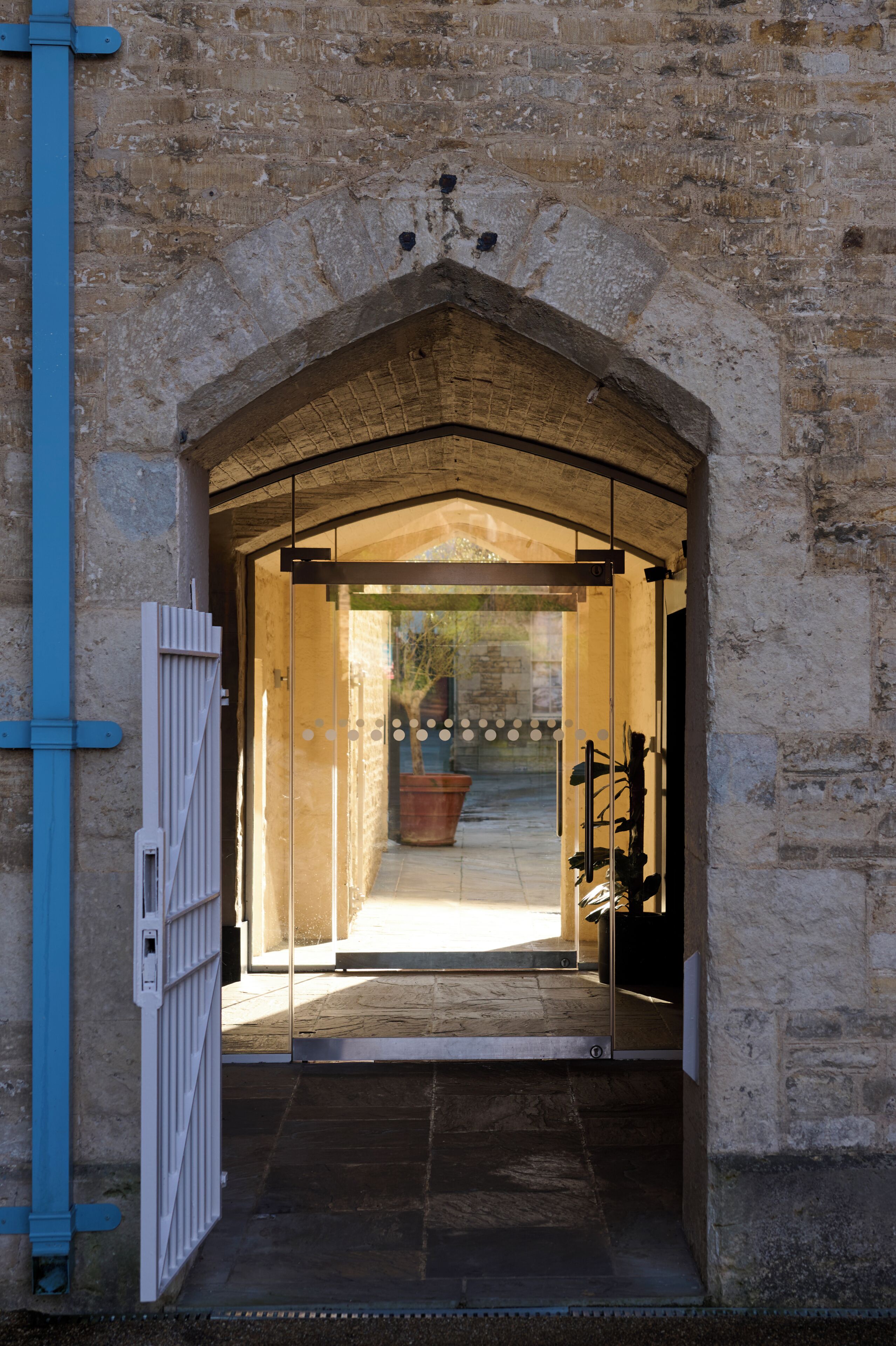 An arched stone entrance to a building with a glass door, a metal gate, and a pathway leading inside.