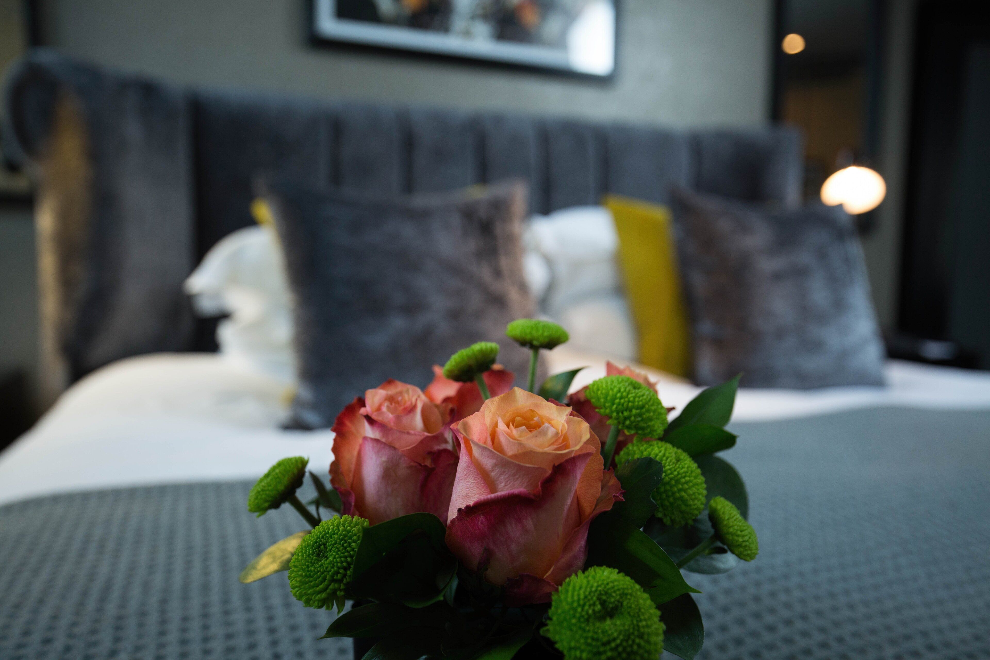 Una cama con edredón blanco, un ramo de rosas y un cabecero gris en una habitación de hotel.