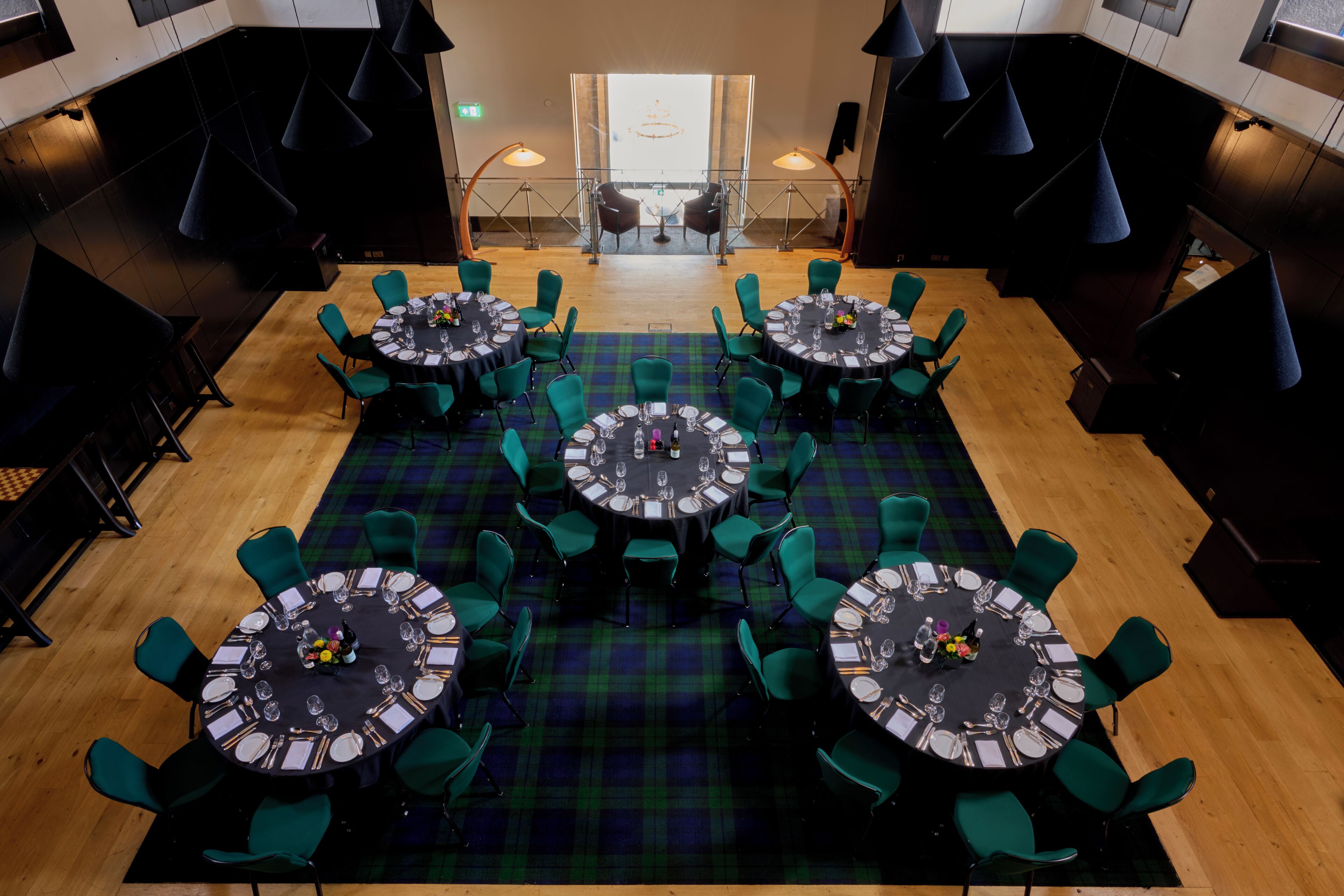 A restaurant with round tables, green chairs, and a plaid carpet.