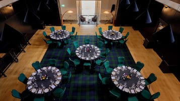 A restaurant with round tables, green chairs, and a plaid carpet.
