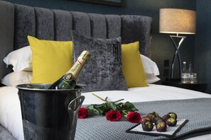 A bed with a champagne bottle in a bucket, a tray of chocolate-covered strawberries, and a bouquet of red roses. - Malmaison Oxford (Oxford)