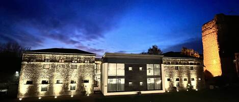 A historic building with stone walls and a modern extension, illuminated at night.