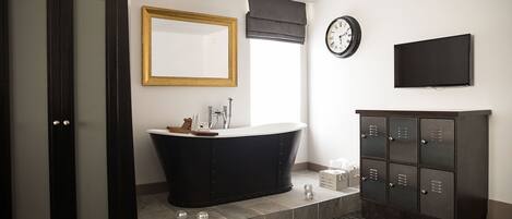 A modern bathroom with a freestanding bathtub, a large mirror, a clock, and a television mounted on the wall.
