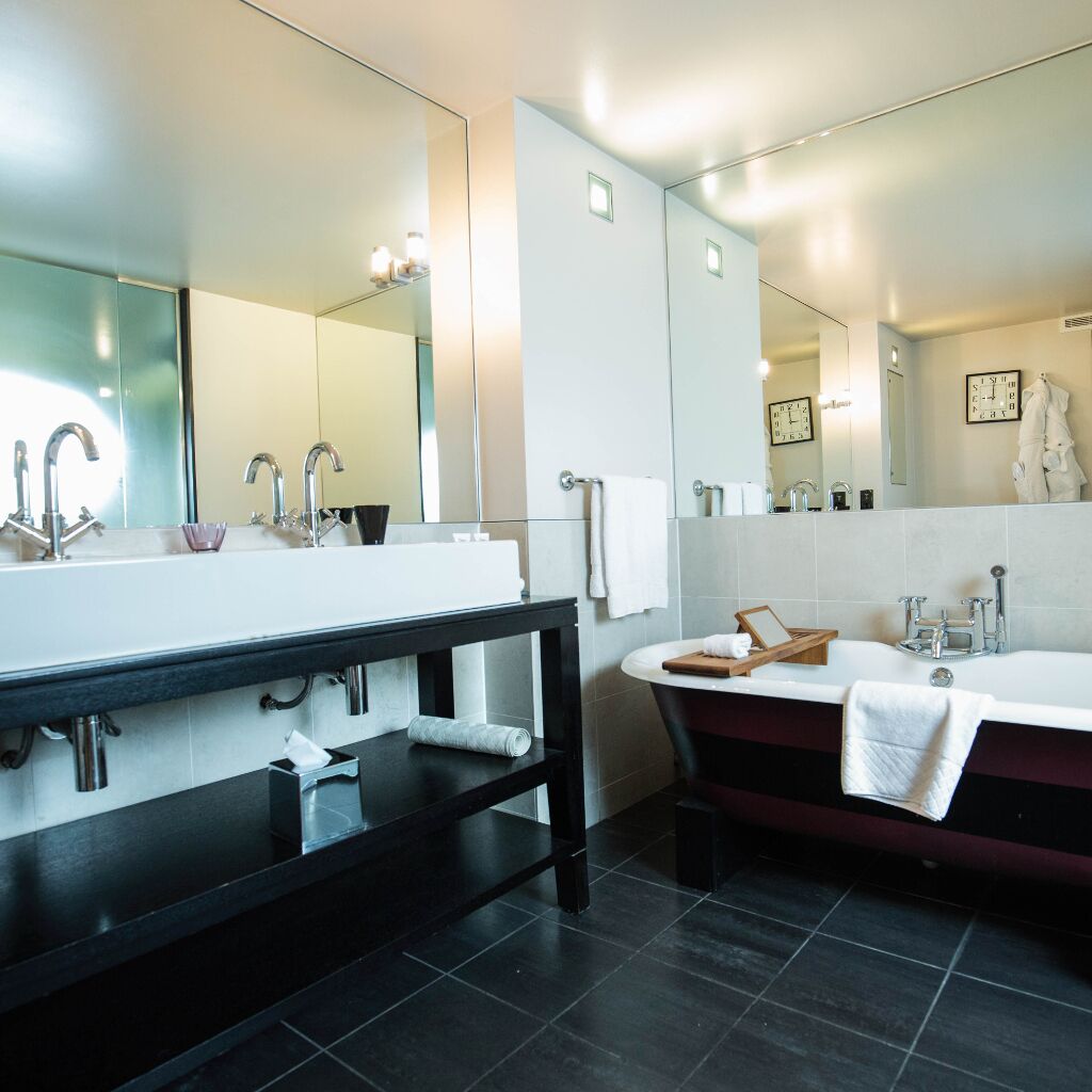 Un baño moderno con un espejo grande, dos lavamanos, una bañera y un mueble de tocador con perchero.