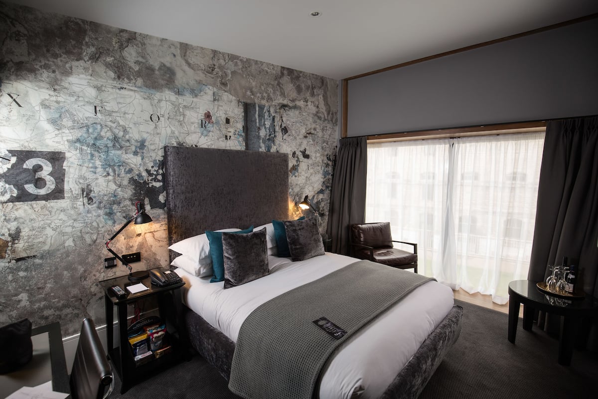 A modern hotel room with a large bed, a map wall, a desk, and a view of the outdoors.