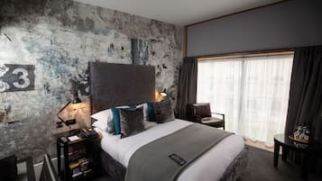 A modern hotel room with a large bed, a map wall, a desk, and a view of the outdoors.
