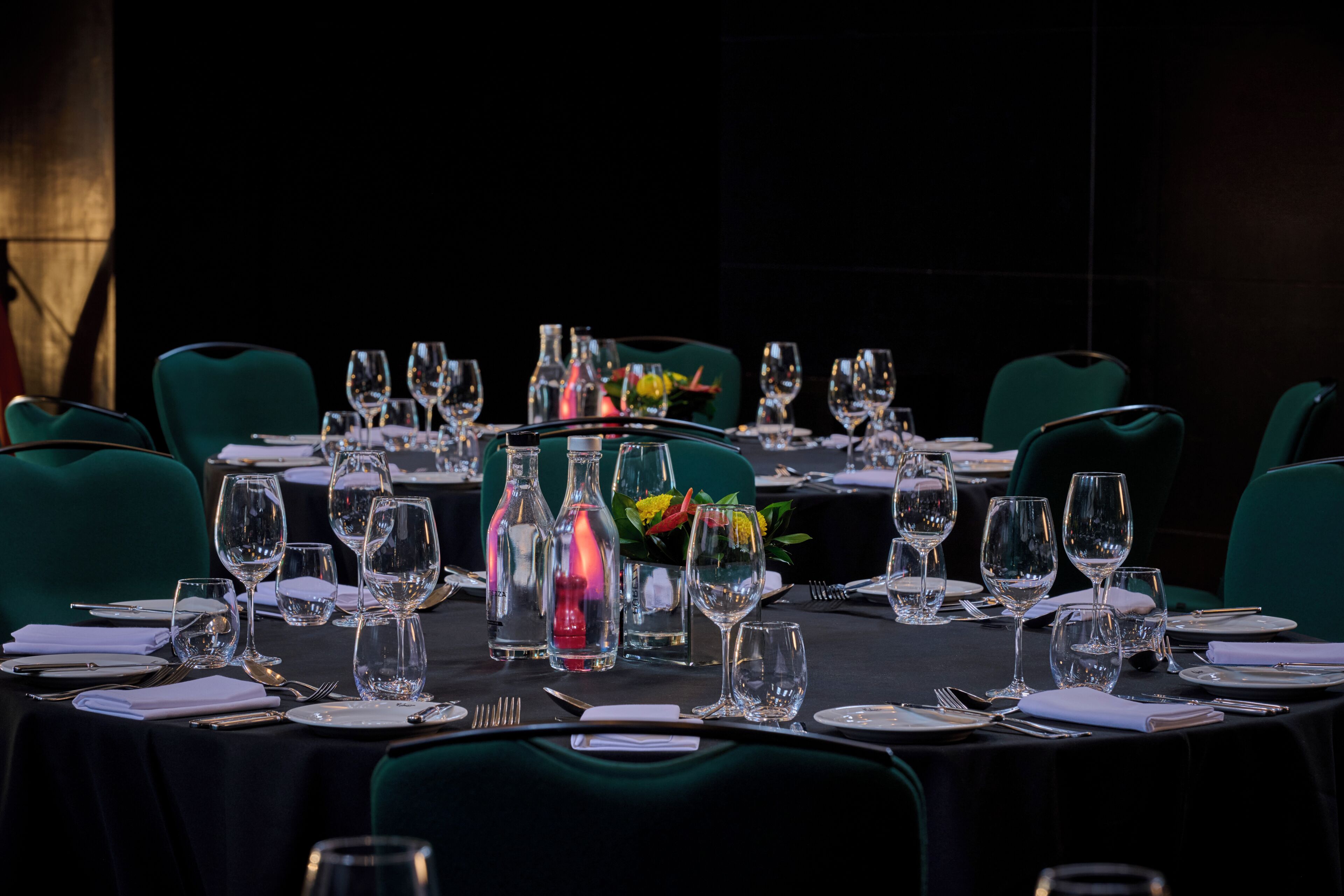 A dining table set with multiple chairs, glasses, and cutlery, with a vase of flowers in the center.