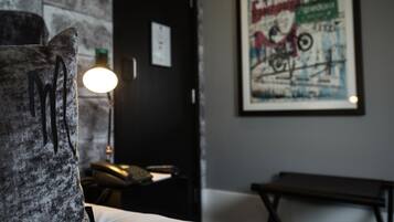 Una habitación con una cama, un escritorio con lámpara, un cartel enmarcado en la pared y un banco.
