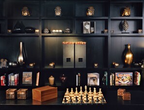 A dark-themed room with shelves containing decorative items, a chessboard, and books. - Malmaison Oxford (Oxford)