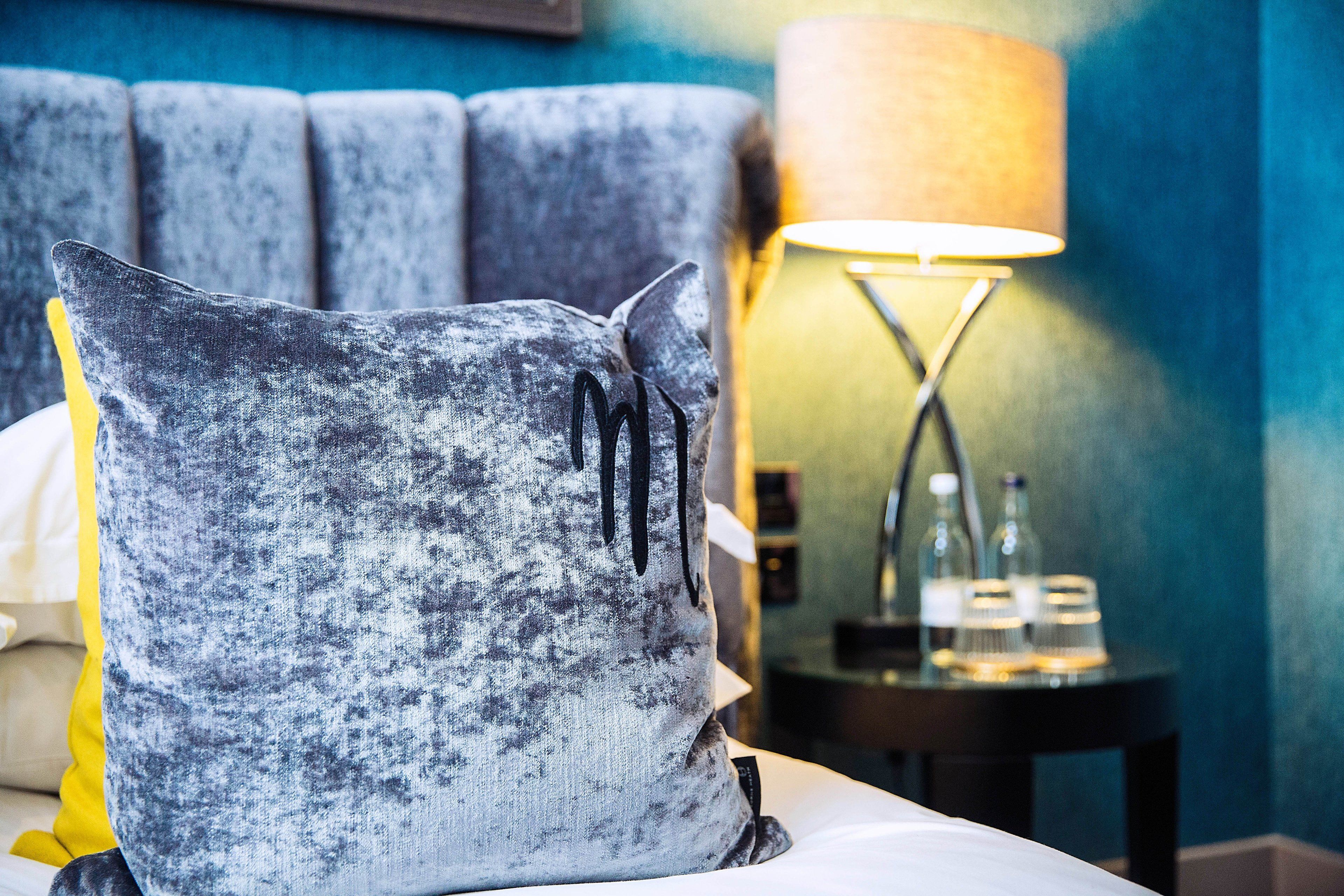 A bed with a grey textured pillow and a bedside lamp with a yellow lampshade.
