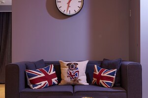 Ein Wohnzimmer mit einer Couch, zwei Kissen mit Union-Jack-Motiven und einer Wanduhr.