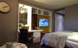 Una habitación de hotel con una cama, un escritorio con una silla, un televisor y un reloj en la pared.