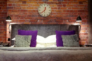 Ein Bett mit Backsteinwand im Hintergrund, einer Uhr und zwei Lampen.
