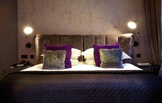 Ein Bett mit gesteppter Bettdecke, zwei Kissen und zwei Wandlampen.