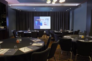 A conference room with multiple tables, chairs, and a large screen displaying a presentation.