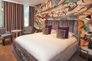 Ein Hotelzimmer mit einem großen Bett, zwei Sesseln, einem kleinen runden Tisch und einem dekorativen Kopfteil.