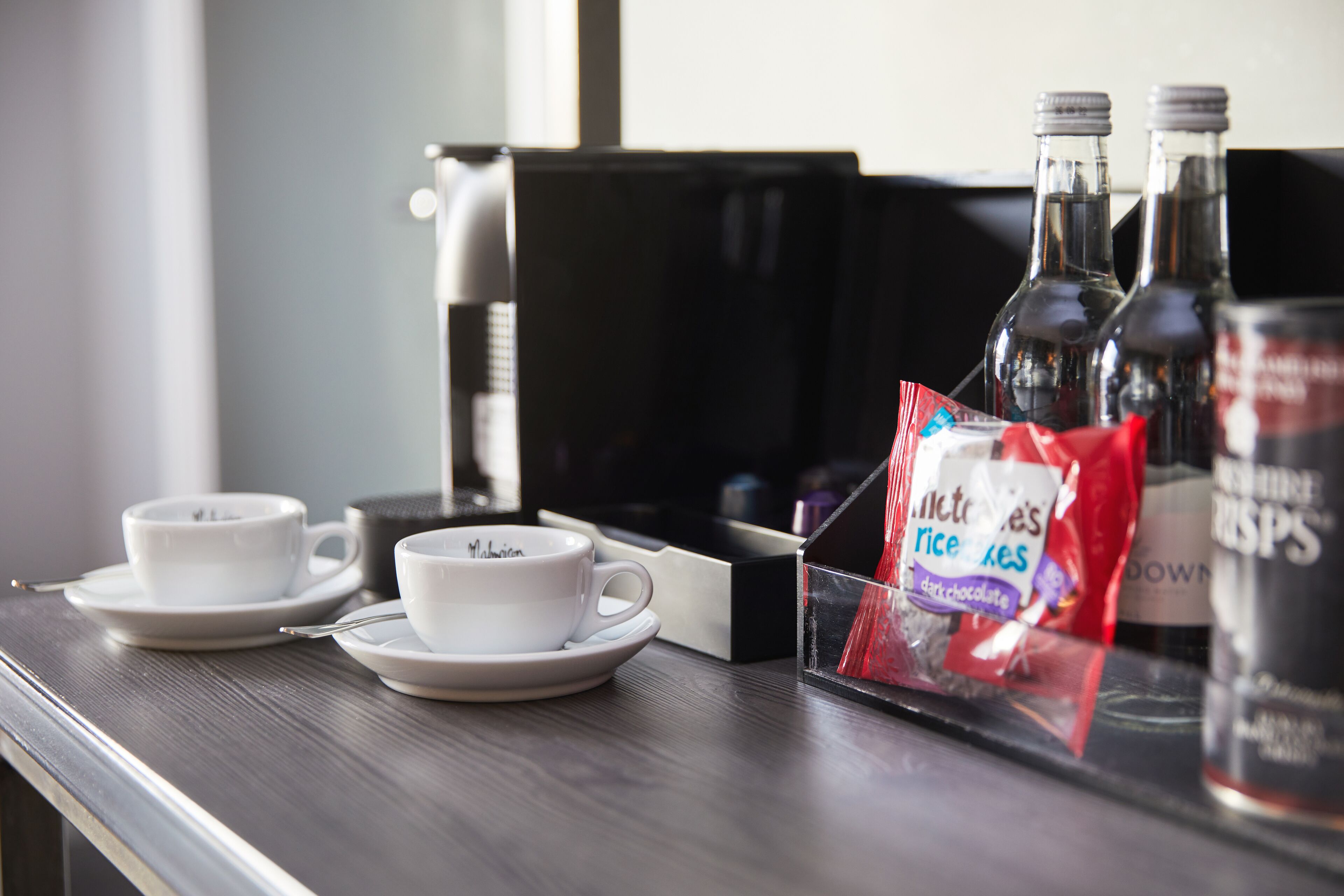 A breakfast tray with two white cups, a small box, and two bottles of syrup.