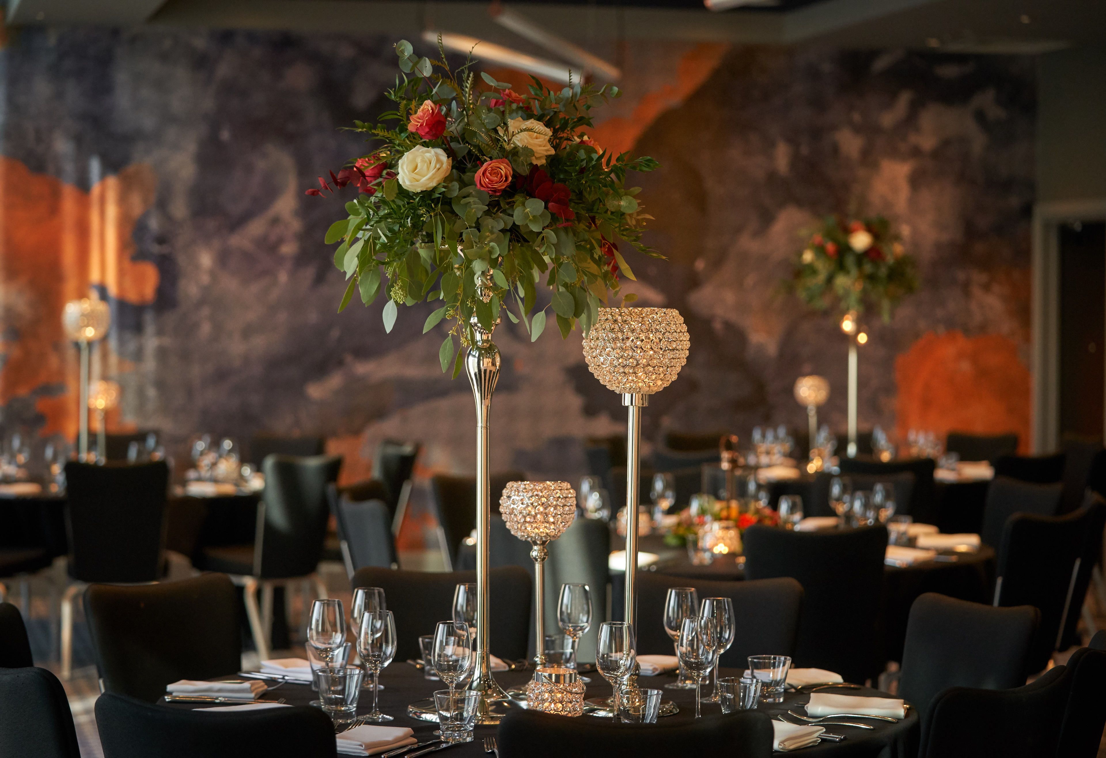 A restaurant setting with tables set for dining, featuring floral centerpieces and crystal candle holders.