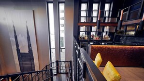 A bar area with a high ceiling, large windows, and a staircase leading to an upper level. - Malmaison Liverpool (Liverpool)
