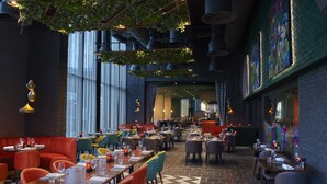 A restaurant with high ceilings, hanging plants, and a mix of red and grey seating. Tables are set with wine glasses and plates. - Malmaison Liverpool (Liverpool)