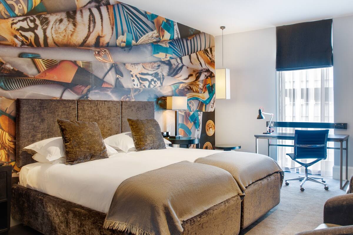 A hotel room with a large bed, two pillows, a desk with a chair, and a window with curtains.